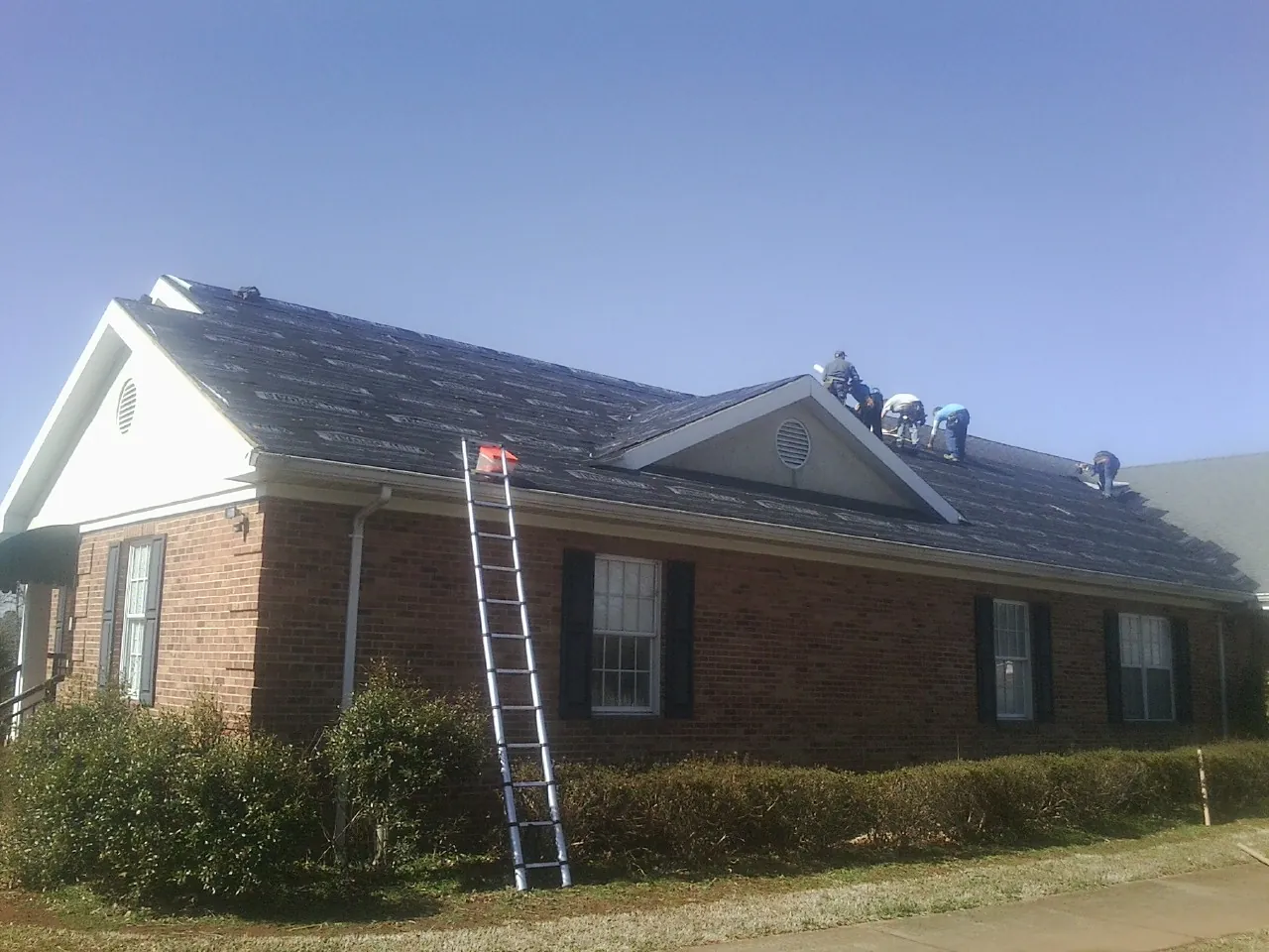 Crew tearing shingles off a brick ranch roof with a ladder set — Emergency Roof Repair work by our crew in Alton