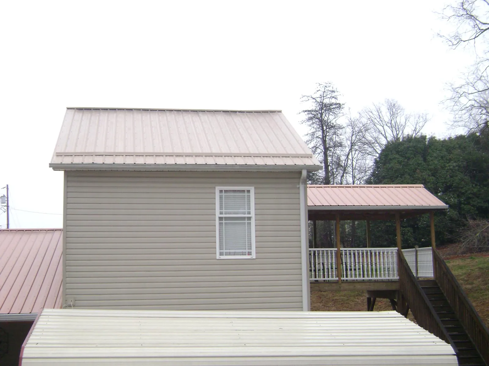 Tan metal roofs on a two story addition and attached porch, from a Roof Replacement job in Alton